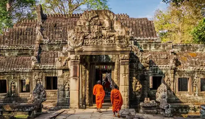 Två munkar i orange klädnader som går i ett tempel i Kambodja