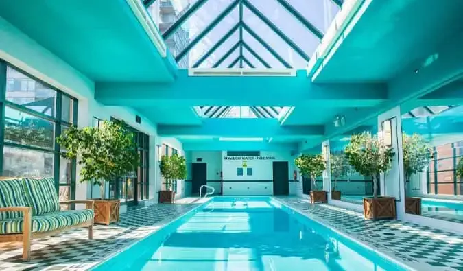 Isang mahabang panloob na swimming pool na may linya na may maliliit na nakapaso na puno sa isang glass atrium sa Yorkville Royal Sonesta hotel sa Toronto, Canada