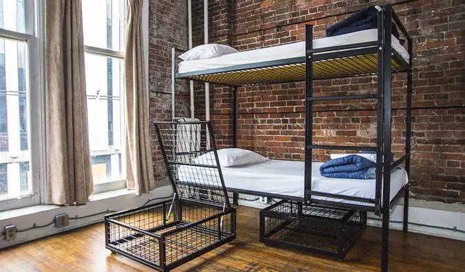 Dortoir avec lits superposés en métal de style industriel, grandes fenêtres et murs en briques apparentes au Cambie Hostel Gastown, Vancouver