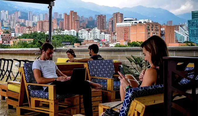 Folk som sitter på utendørsterrassen med Medellins skyline i bakgrunnen på Los Patios hostel i Medellin