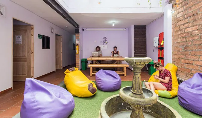 Area umum dengan bean bag ungu dan kuning dan orang-orang yang bekerja menggunakan laptop di Purple Monkey, Medellin