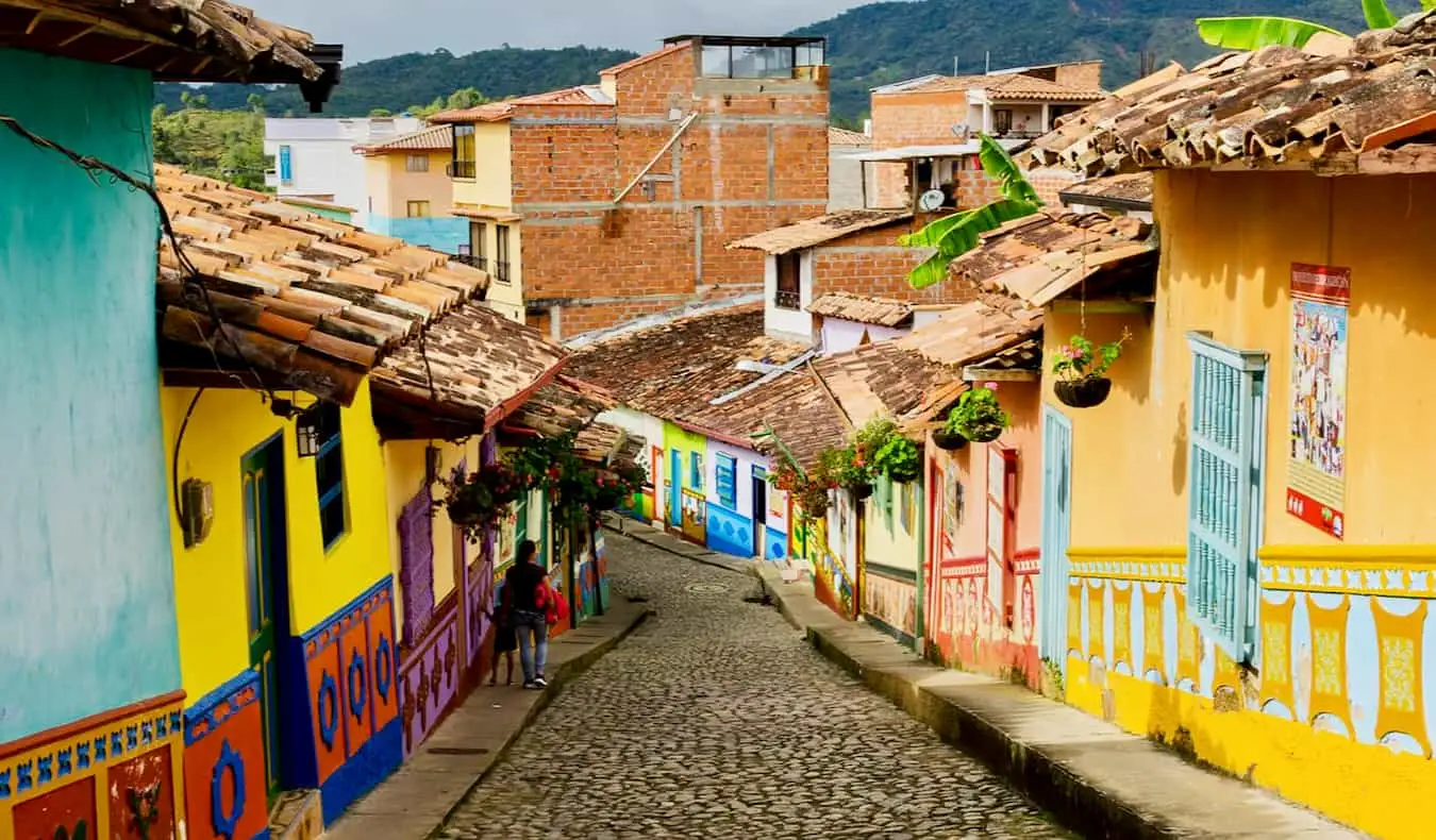 Una vista de una amplia plaza rodeada de edificios históricos de color naranja brillante con el puerto y modernos rascacielos al fondo en Cartagena, Colombia