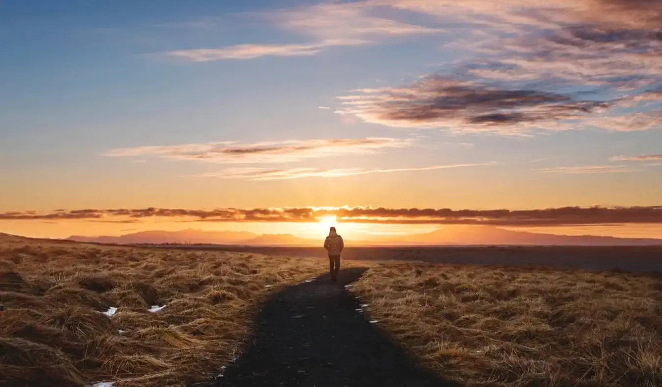 Um viajante caminhando ao pôr do sol em uma trilha no exterior