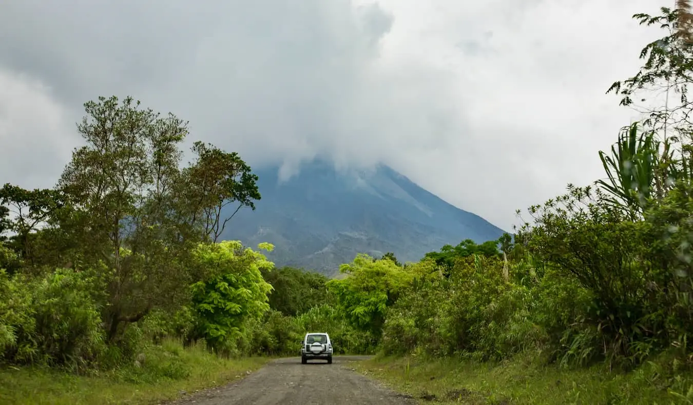 Um carro dirigindo em uma estrada de terra à sombra do vulcão Arenal, na Costa Rica