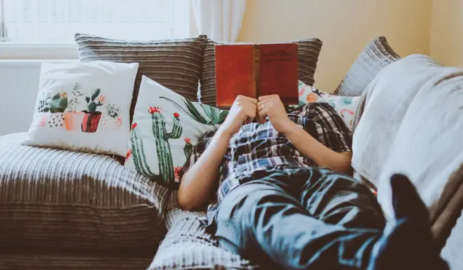 Een man die een boek leest terwijl hij op zijn bank zit