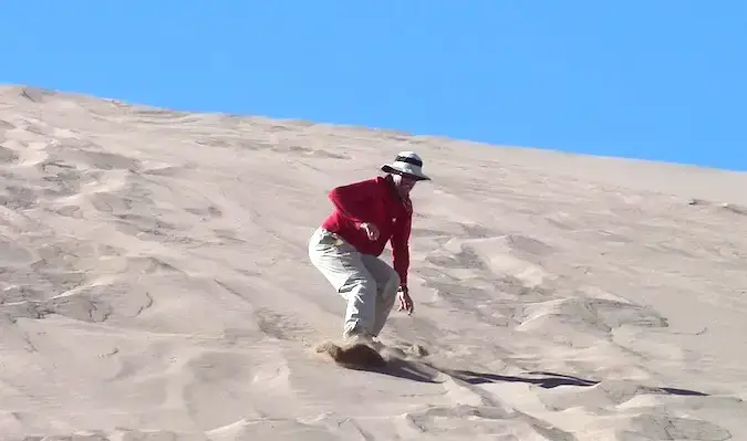 Een 50-jarige reiziger sandboardt een zandduin af