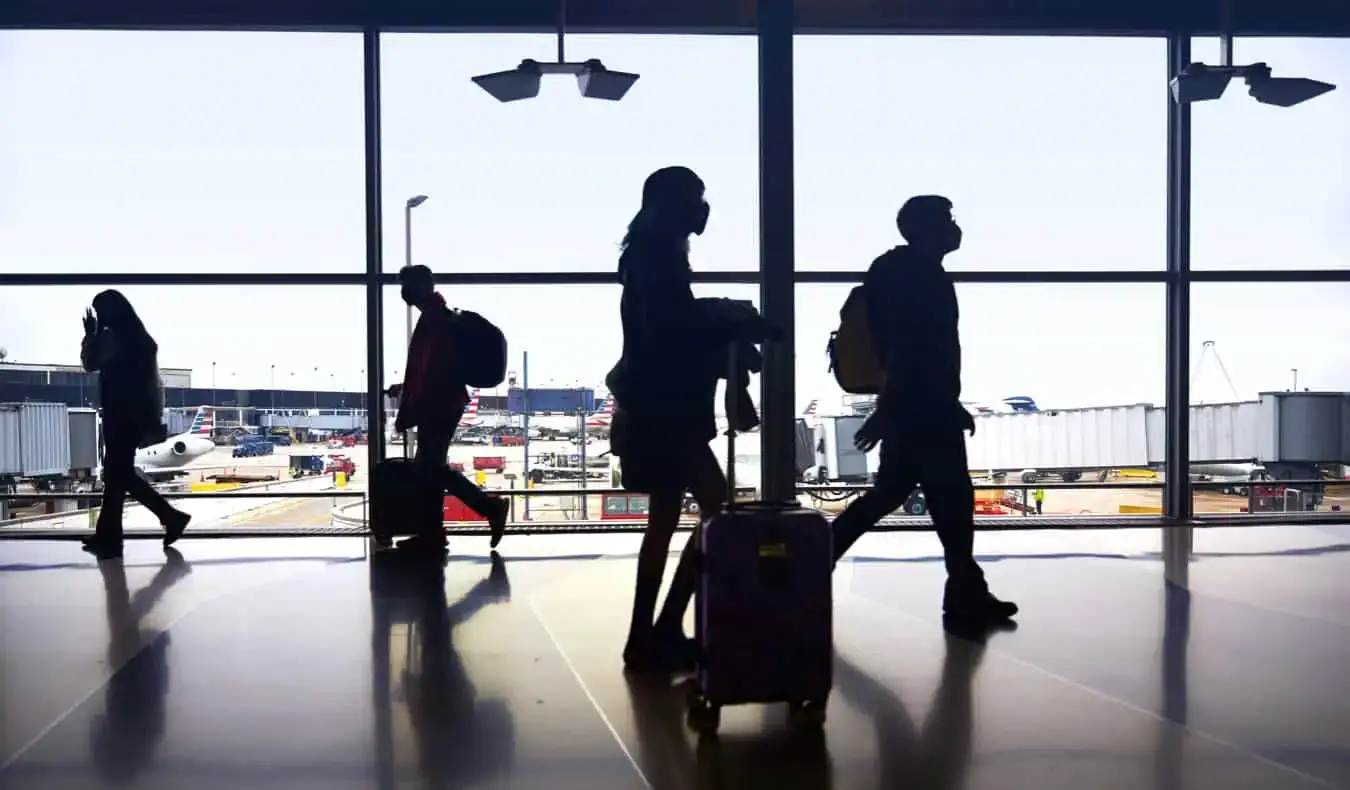 mensen silhouet door een raam op een luchthaven terwijl ze naar hun gate lopen