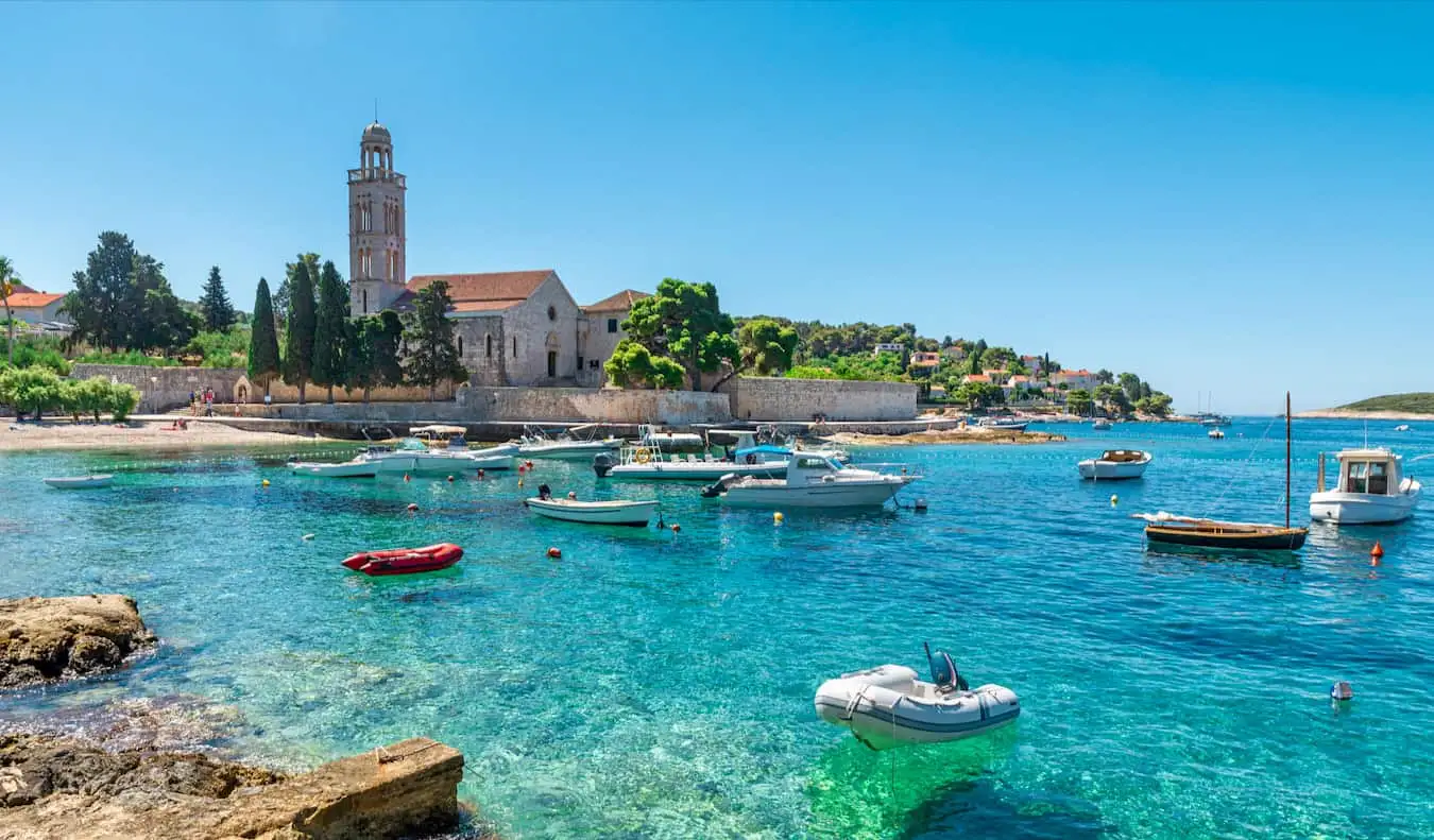 Arka planda eski binaların olduğu güneşli bir yaz gününde Hvar, Hırvatistan'daki bir körfezdeki güzel sular