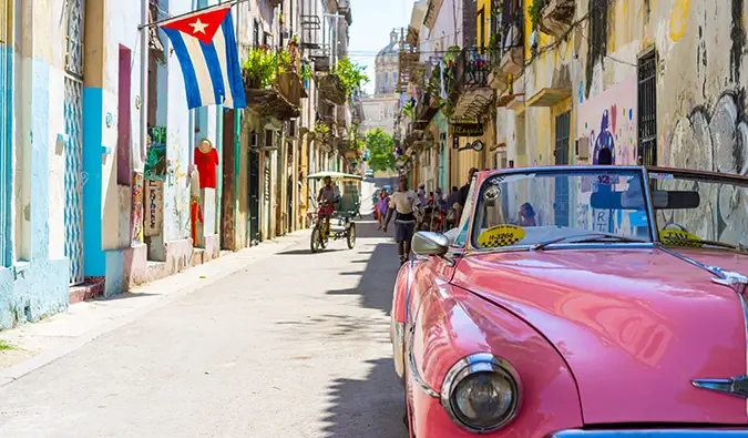 een klassieke roze auto in Cuba in een drukke straat