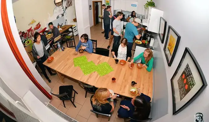 Foto in stile fisheye della cucina dell'Onefam di Praga, con persone sedute a un tavolo che preparano il cibo, mangiano e parlano.