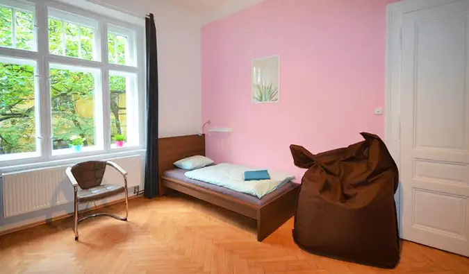 Camera con pareti rosa, poltrona a sacco, letti gemelli e grandi finestre al Travel and Joy Hostel di Praga