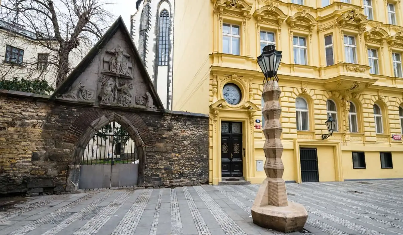 Kubistische lantaarnpaal voor een historisch geel gebouw en een poort met poorten, in Praag, Tsjechië