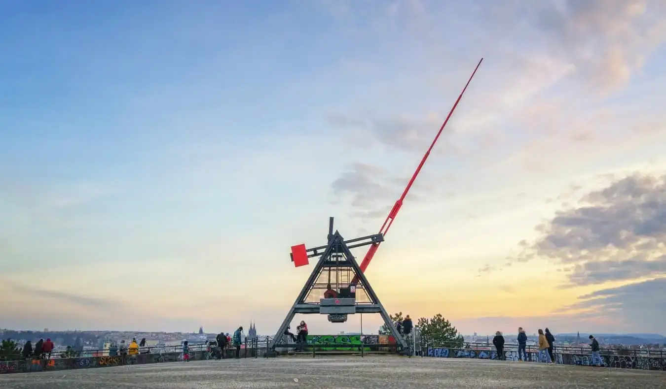 Un metrónomo de metal gigante con la larga mano roja apuntando al cielo al atardecer, en Praga, República Checa