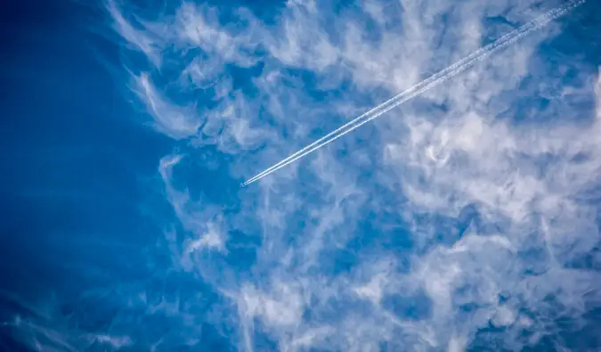 Un avión comercial en lo alto del cielo, cortando las nubes y un cielo azul.