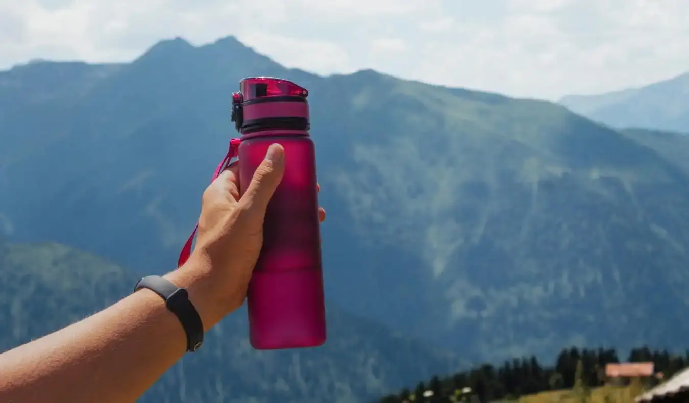 Pessoa segurando uma água reutilizável magenta em um cenário montanhoso