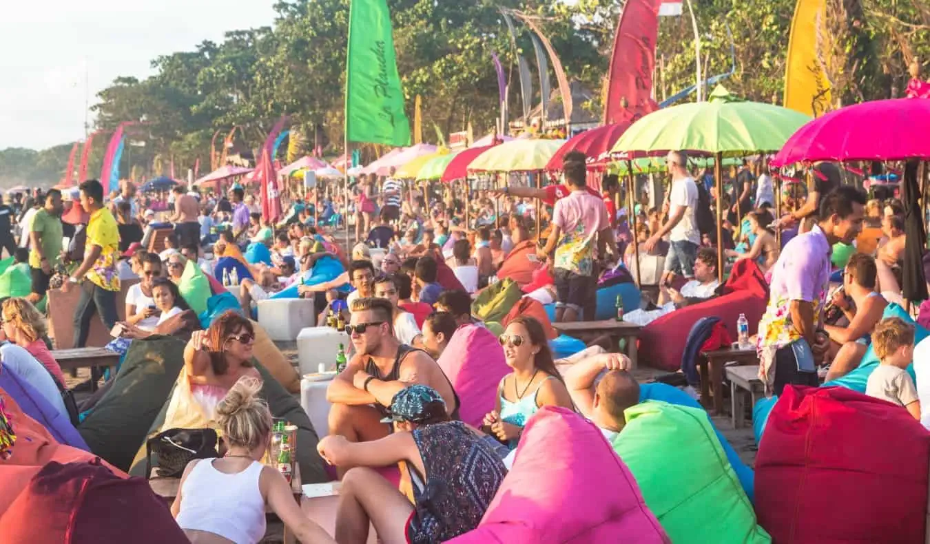 Praia completamente lotada de turistas sentados em pufes em Bali, Indonésia