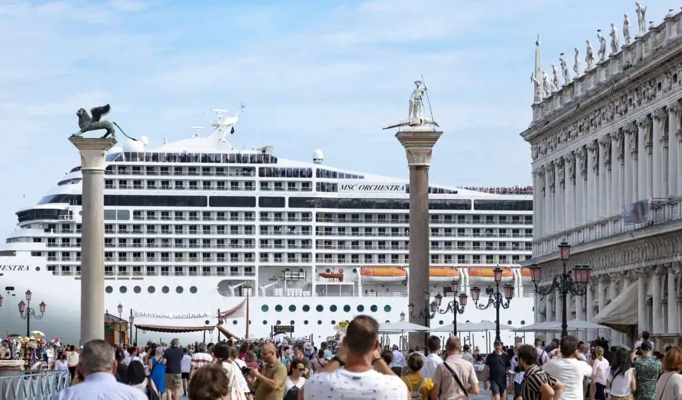 O navă de croazieră planează mare deasupra pieței istorice Piazza San Marco din Veneția, Italia, în timp ce mulțimile de turiști fac fotografii în prim plan