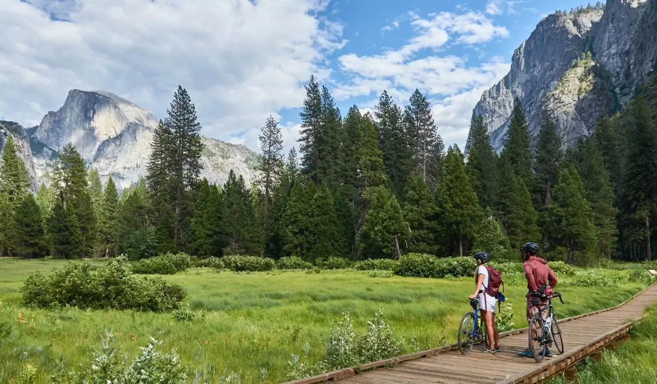 Duas pessoas de bicicleta param e admiram a paisagem de florestas e montanhas no Parque Yosemite, nos Estados Unidos