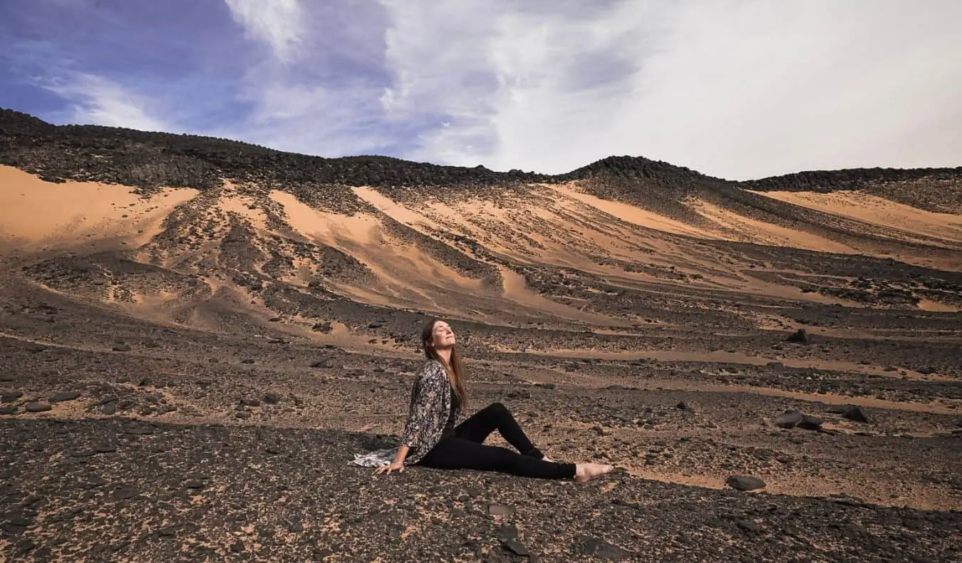 Monica, una viatgera en solitari, asseguda al desert d'Egipte posant per a una foto