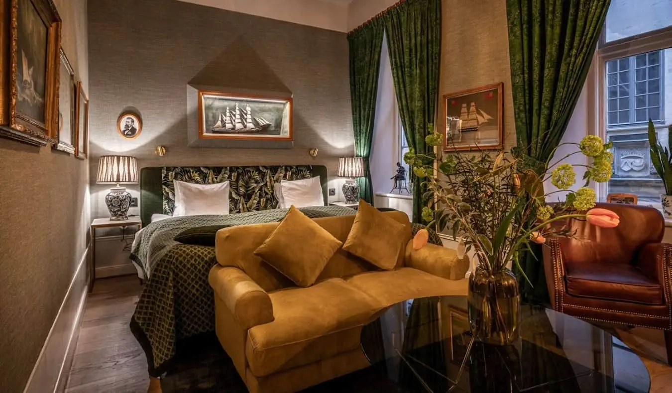 Kamar tamu mewah dengan sofa beludru, kursi santai dari kulit, tirai zamrud di jendela, dan dinding berlapis kain di Collectors Victory Hotel di Stockholm, Swedia