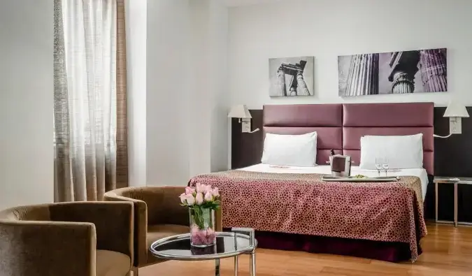 Une chambre aux accents roses, notamment des roses dans un vase sur une table basse de l'hôtel Eurostars Roma Aeterna à Rome, en Italie