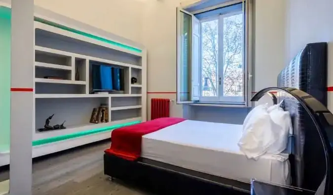 Isang simpleng guestroom na may kama sa tapat ng entertainment center kabilang ang mga istante at TV sa Luxury on the River hotel sa Rome, Italy