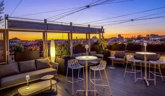 Bar y salón en la azotea con el paisaje urbano al fondo justo después del atardecer en el Monti Palace Hotel en Roma, Italia