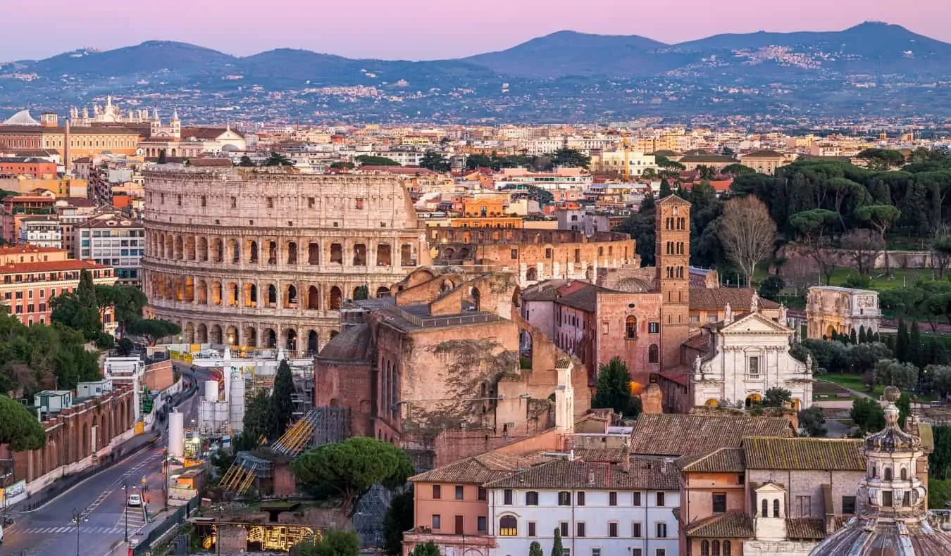 El horizonte de Roma, Italia al atardecer, con edificios históricos como el Coliseo en primer plano y montañas al fondo