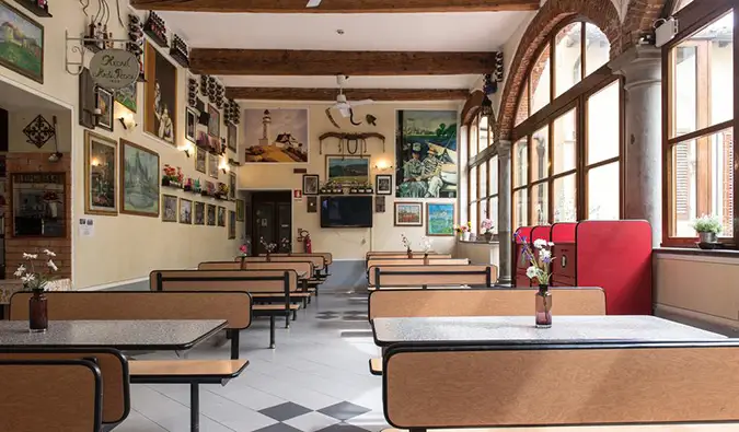 Cafeteriabereich mit vielen langen Tischen, Kunst an den Wänden und Bogenfenstern im Archi Rossi Hostel in Florenz, Italien