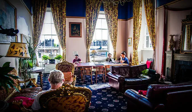 Salle commune confortable avec canapés en cuir, grands fauteuils, table commune et grandes fenêtres à Castle Rock à Édimbourg