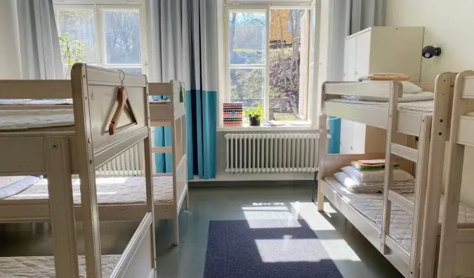 Dormitori a l'Hostel Suomenlinna a Hèlsinki, Finlàndia, amb lliteres de fusta blanca i llum natural que entra.