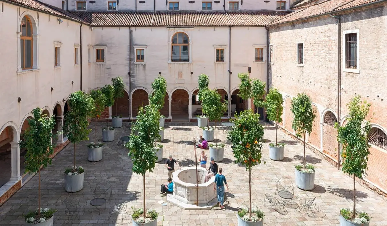 Historický klášter plný pomerančovníků a lidí stojících kolem chatování v Combo Venezia, hostelu v italských Benátkách.