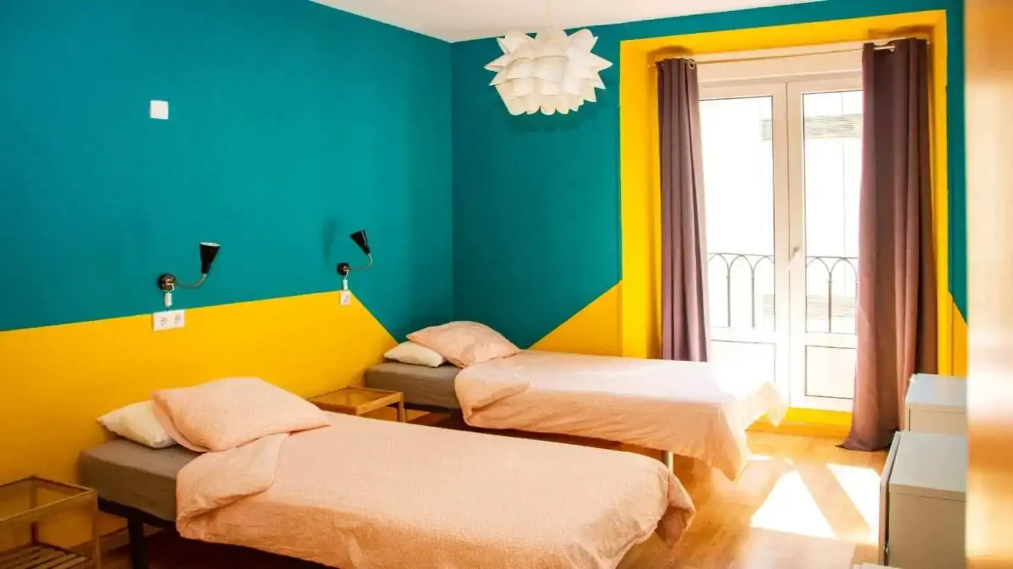 Dua tempat tidur kembar di kamar bercat cerah di hostel Sungate One di Madrid, Spanyol.