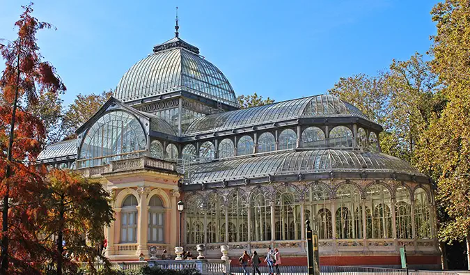 Menschen stehen an einem sonnigen Tag vor dem Kristallpalast und dem Brunnen im Retiro-Park, Madrid, Spanien