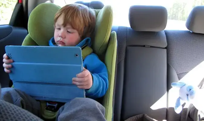 Tout-petit jouant avec des appareils électroniques sur la banquette arrière lors d'un road trip en famille