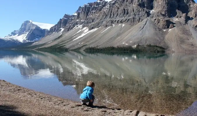 Un niño pequeño se inclina para tocar el hermoso lago en el extranjero