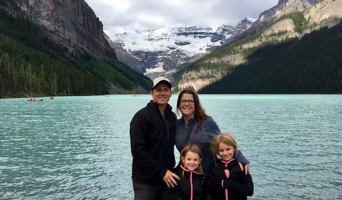 Amanda et sa famille voyageuse posant près d'un lac avec des montagnes en arrière-plan