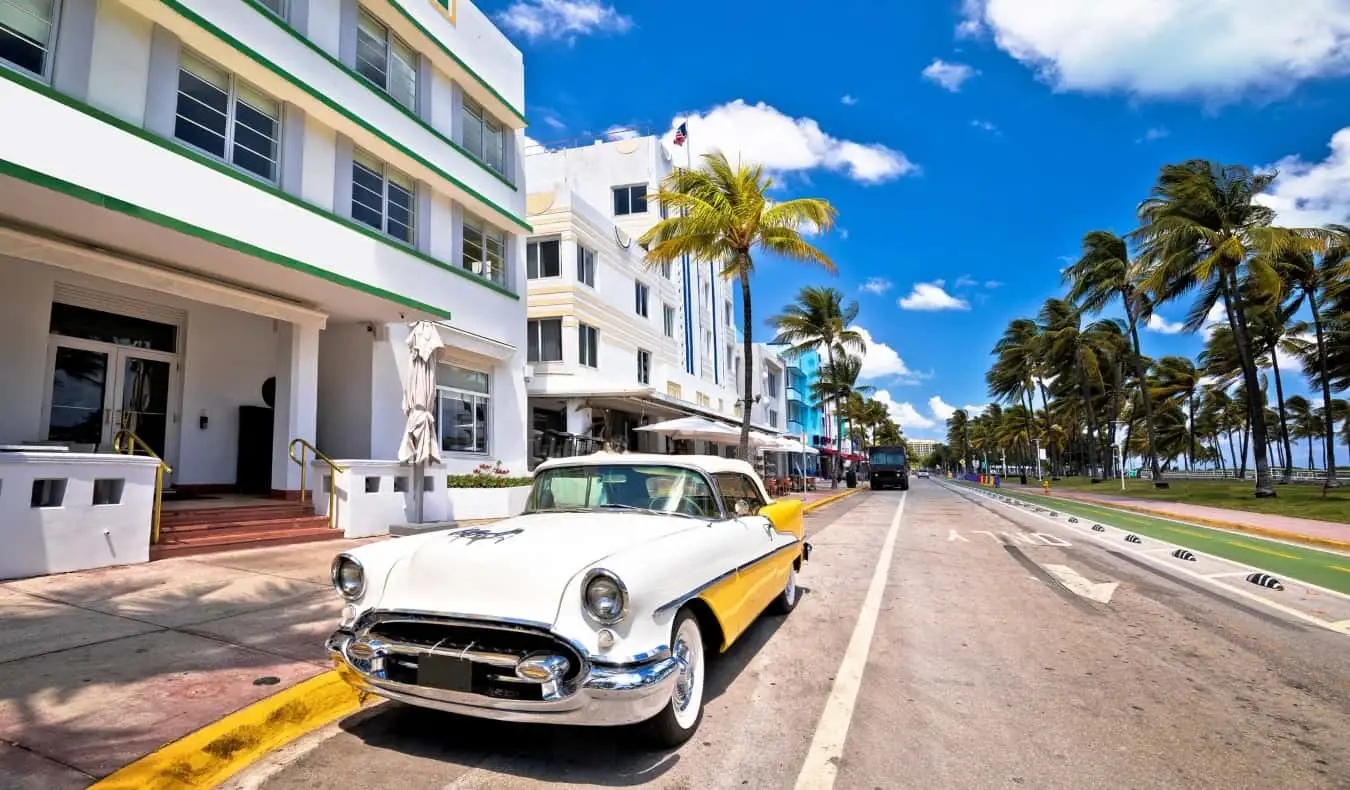 Krāsains, vecs 1960. gadu automobilis uz ielas pretī Art Deco ēkām South Beach pilsētā Maiami, Floridā