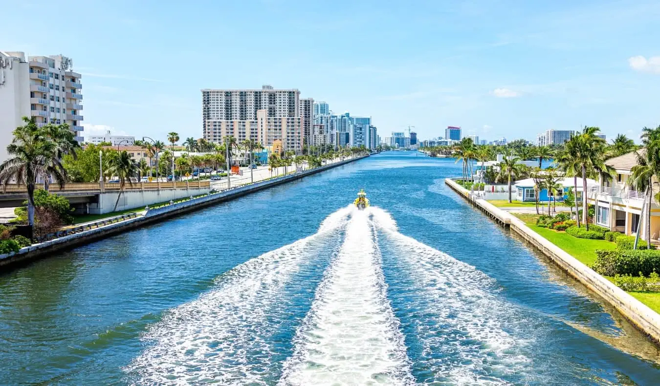 Loď pluje po velkém kanálu lemovaném obytnými domy a palmami v Miami na Floridě