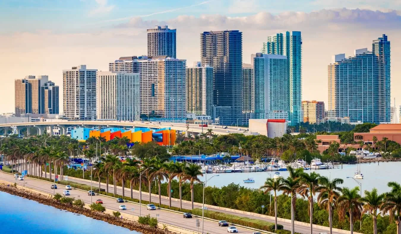 L'horizon du centre-ville de Miami au coucher du soleil, avec des gratte-ciel en arrière-plan et un boulevard bordé de palmiers au premier plan