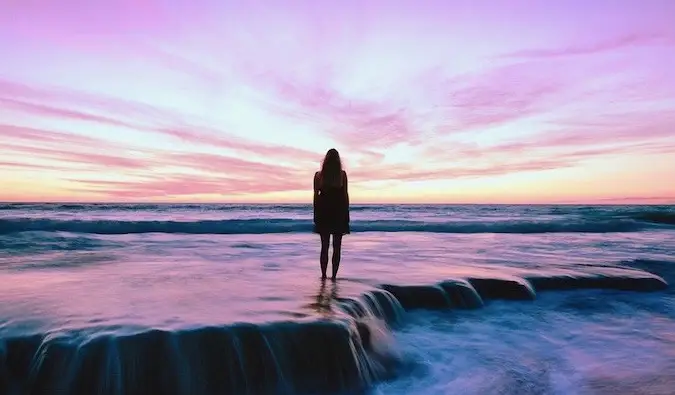 ビーチの浅瀬に立って明るい夕日を眺める女性