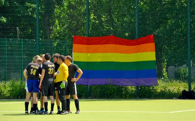 Sebuah tim sepak bola berdiri di lapangan dengan bendera kebanggaan besar di latar belakang