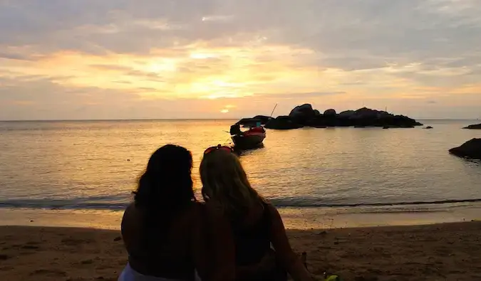 Dua wanita bersama di pantai di luar negara pada waktu matahari terbenam