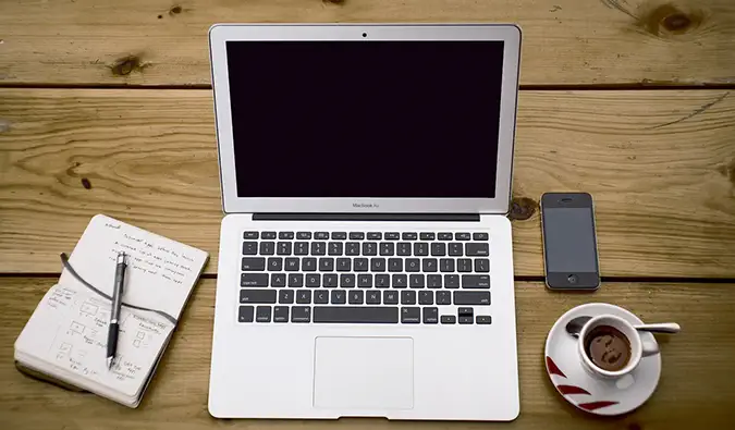 Una foto de una computadora portátil sobre un escritorio de madera con una libreta y una taza de café