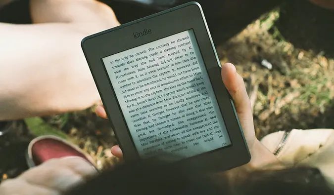 Popotnik, ki sedi v travi in ​​bere e-bralnik Kindle