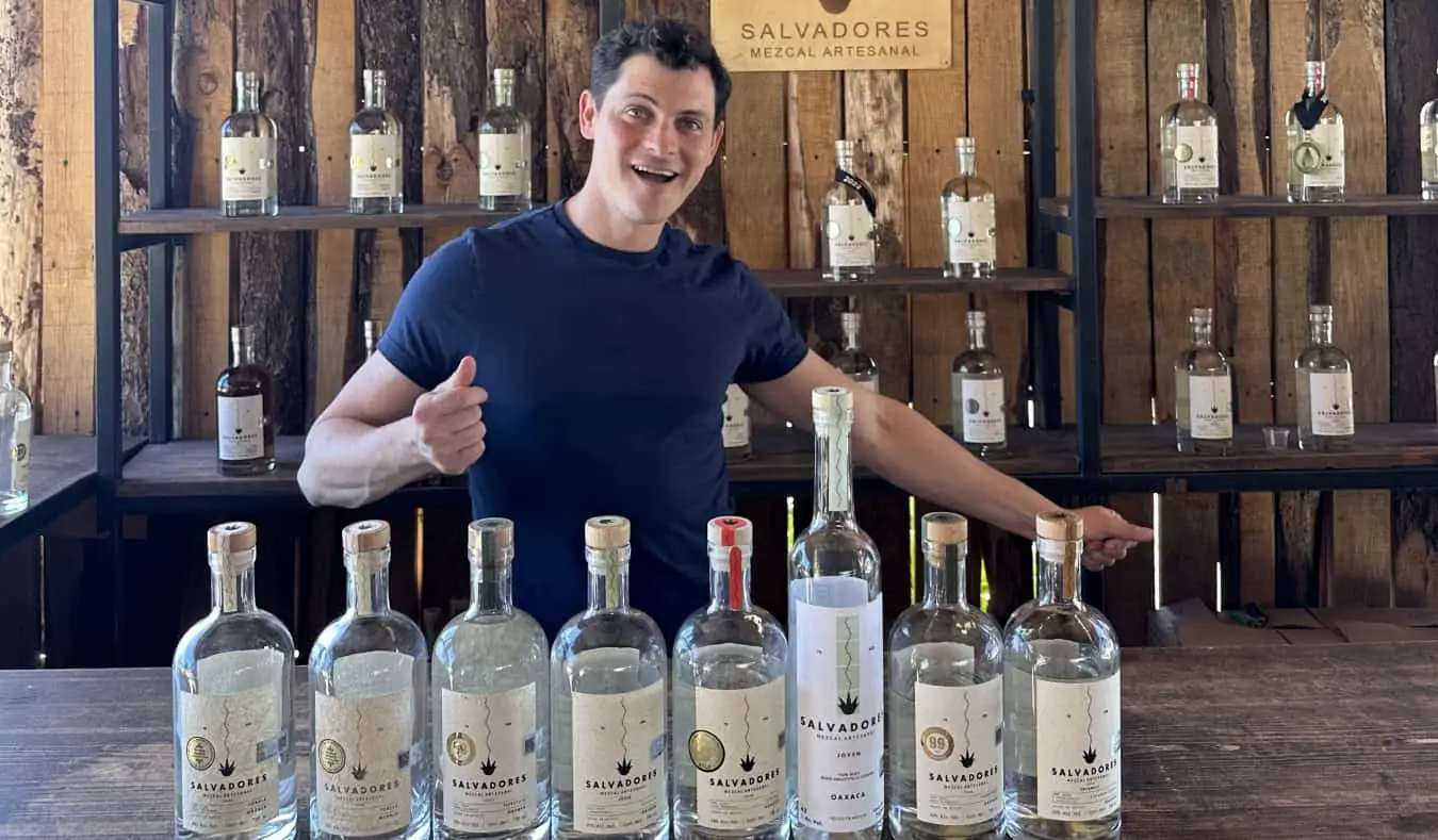 Nomadic Matt staat voor een rij mezcalflessen in Mexico