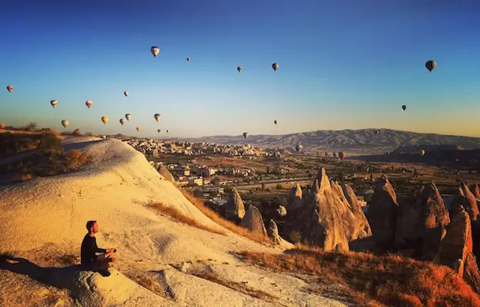 Si Scott Dinsmore ay nakaupo sa isang bato sa Turkey habang pinupuno ng mga hot air balloon ang kalangitan