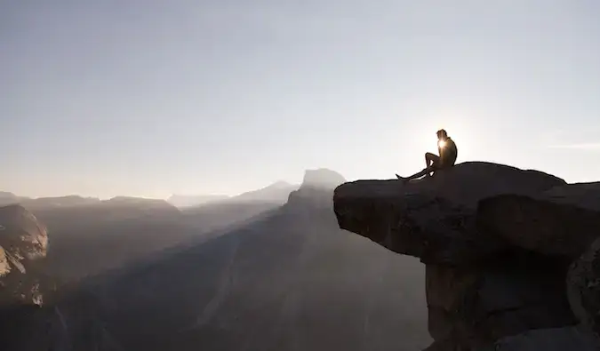 Um viajante solitário sentado à beira de um penhasco pensando durante o pôr do sol