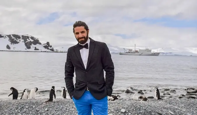 Jon Levy posant pour une photo en Antarctique avec des pingouins à proximité