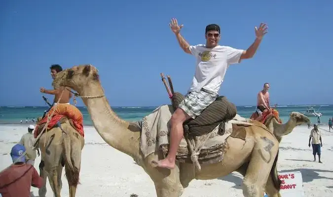 Lee Abbamonte a cavallo di un cammello sulla spiaggia